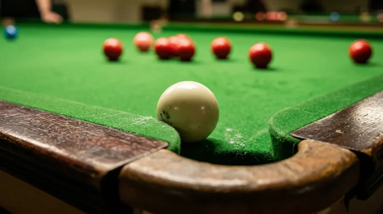 Close-up of a snooker table with scattered red balls and a miscued white ball near the cushion